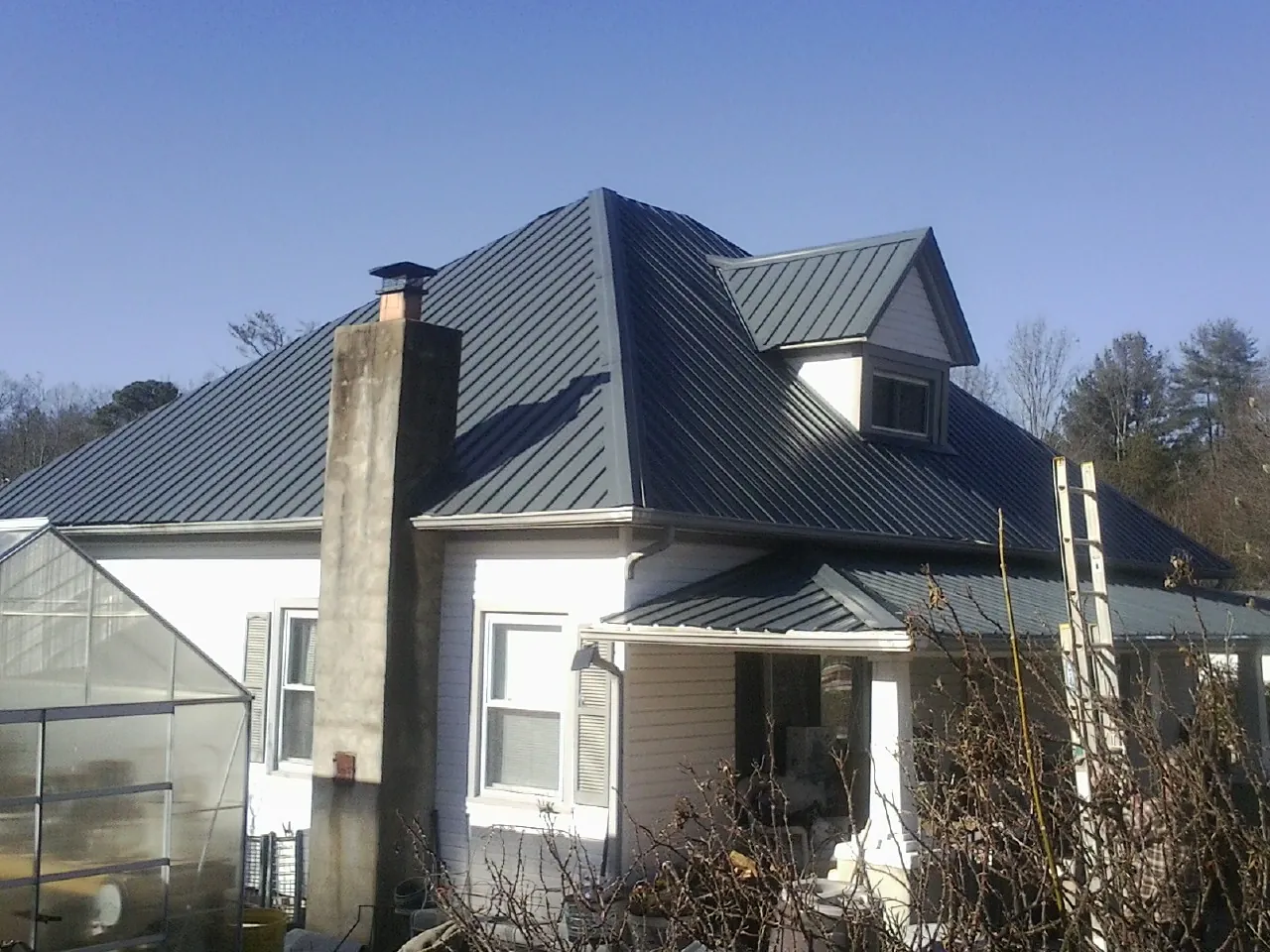 Dark blue standing seam metal roof on a white farmhouse with dormer — Slate & Tile Roof Repair by Roofing Brothers in Mcintosh