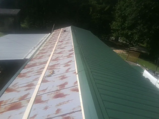Old rusted panels beside newly installed green metal roofing — Wind Damage Roof Repair by Roofing Brothers in Mcintosh