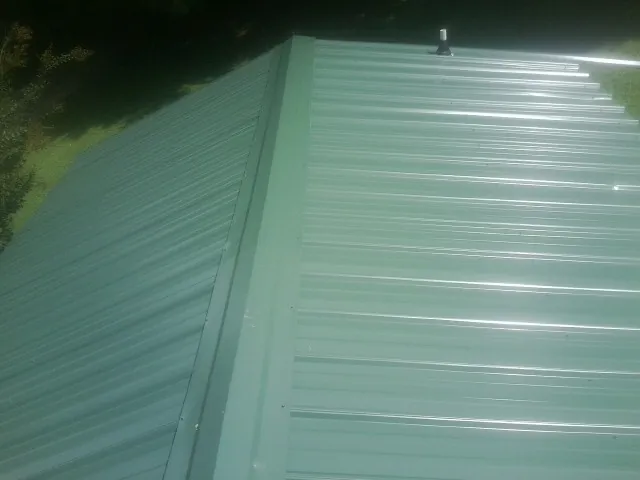 New green metal panels meeting at the ridge of a roof — Flat Roof Repair work by our crew in Mcintosh