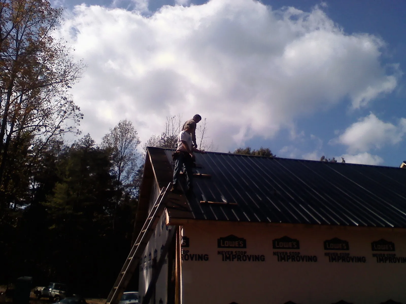 Roofer fastening dark metal panels high against a cloudy sky, from a Roof Inspection job in Mcintosh