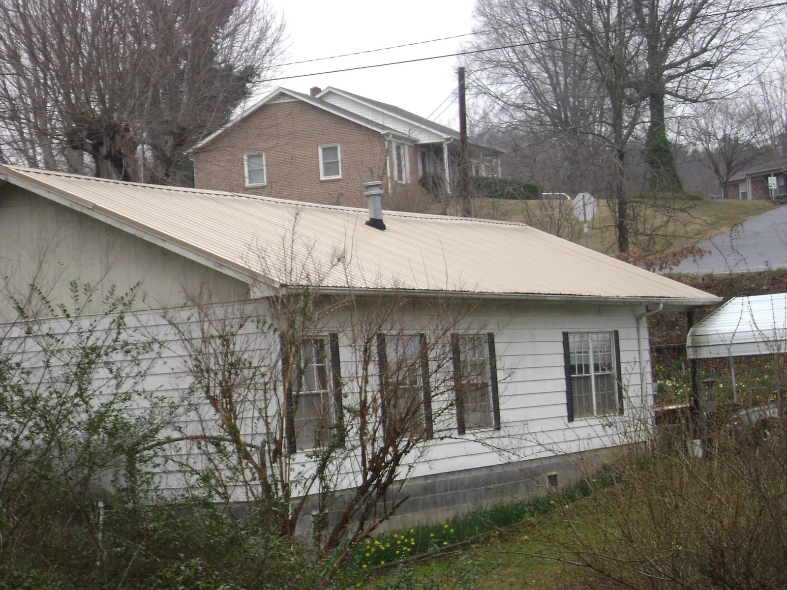 Tan metal roof on a white sided house set into a hillside — Commercial Roofing by Roofing Brothers in Mcintosh
