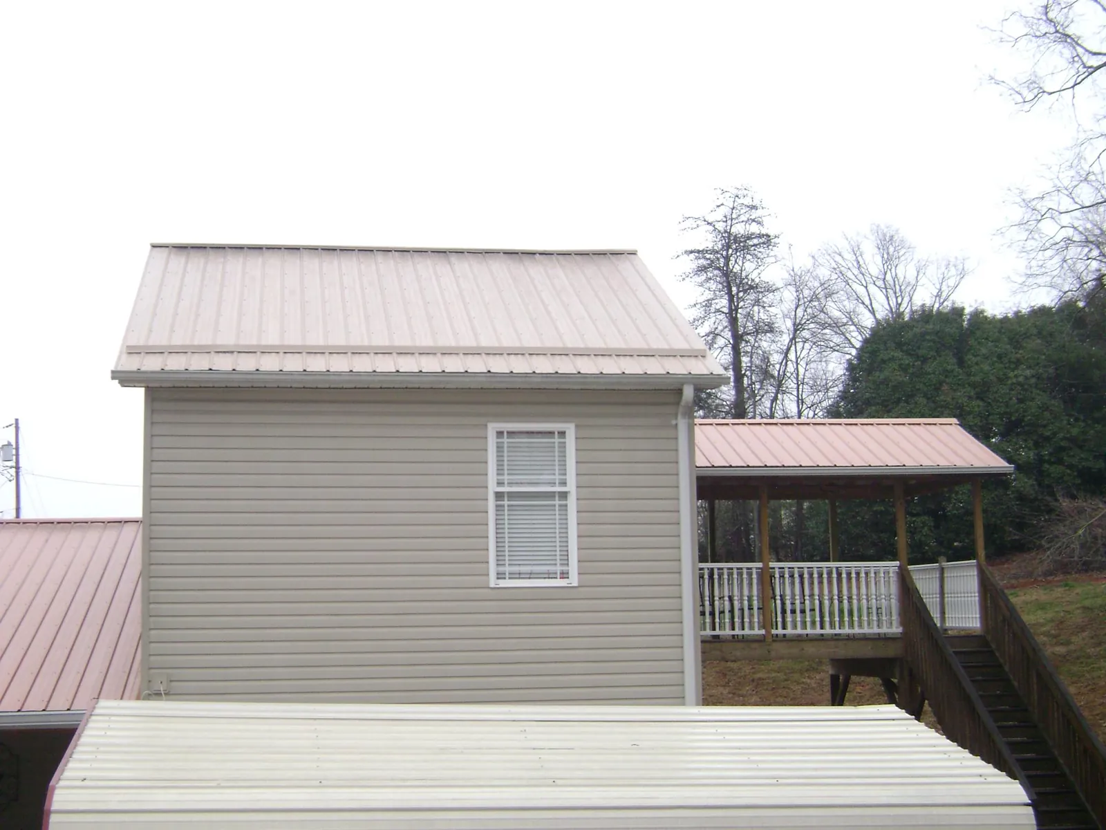 Tan metal roofs on a two story addition and attached porch, from a Roof Replacement job in Mcintosh